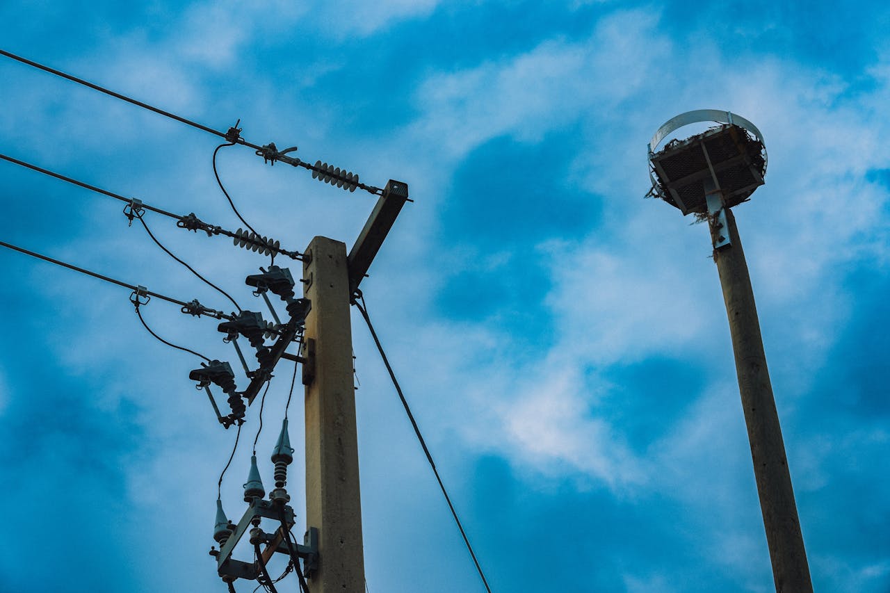 Power lines and a street light silhouette against a cloudy blue sky.