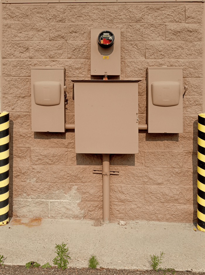 Industrial electrical fuse box with warning stripes on an urban wall.