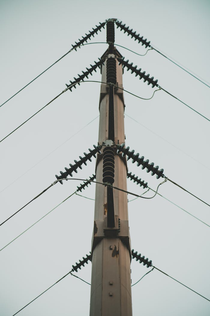 Vertical shot of a high voltage utility pole with electric wires against a clear sky.
